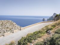 two motorcycles traveling on a narrow paved road by the ocean with mountains in the background