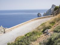 two motorcycles traveling on a narrow paved road by the ocean with mountains in the background