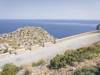 two motorcycles traveling on a narrow paved road by the ocean with mountains in the background