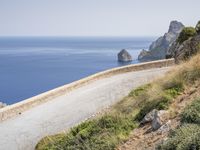 two motorcycles traveling on a narrow paved road by the ocean with mountains in the background