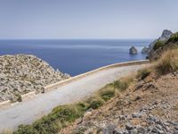 two motorcycles traveling on a narrow paved road by the ocean with mountains in the background