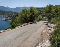 a winding asphalt road with a view of a lake and mountains in the distance in front of trees