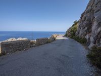 a road is near some cliffs with water in the background and the ocean on the other side