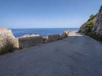 a road is near some cliffs with water in the background and the ocean on the other side