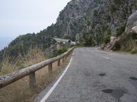 a long and empty road in the middle of the mountains with rocks and woods in the background