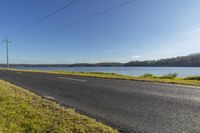 a lone long road with power lines above the water and power poles in the background