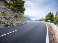 an empty road next to a tall rock wall and forest on the side of the mountain