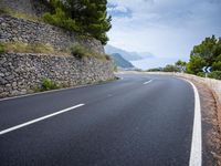 an empty road next to a tall rock wall and forest on the side of the mountain