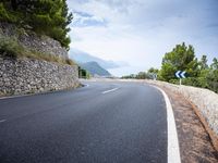 an empty road next to a tall rock wall and forest on the side of the mountain