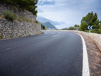 an empty road next to a tall rock wall and forest on the side of the mountain