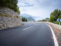 an empty road next to a tall rock wall and forest on the side of the mountain