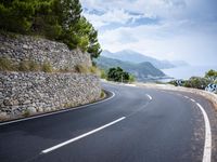 an empty road next to a tall rock wall and forest on the side of the mountain