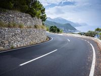 an empty road next to a tall rock wall and forest on the side of the mountain