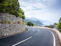 an empty road next to a tall rock wall and forest on the side of the mountain