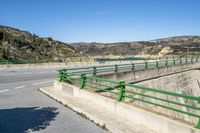 a highway with a dam on one side and mountains on the other side under a blue sky