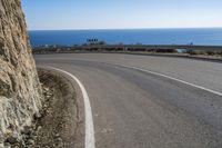 there is a curved road going past the ocean, and sign in english reads a bend