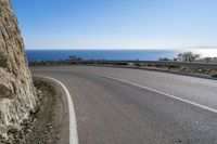 there is a curved road going past the ocean, and sign in english reads a bend