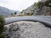 a person riding a motorcycle down a winding road in front of mountains with rocks and boulders on both sides