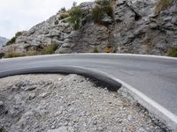 a person riding a motorcycle down a winding road in front of mountains with rocks and boulders on both sides