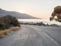 the sun is setting behind some trees and an ocean line road with a man sitting on a motorcycle