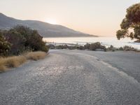 the sun is setting behind some trees and an ocean line road with a man sitting on a motorcycle