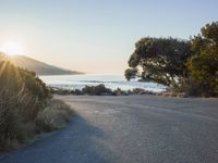 a sunset view from behind the road with a person riding a bike along the shore