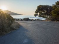 a sunset view from behind the road with a person riding a bike along the shore