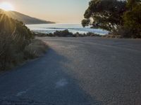 a sunset view from behind the road with a person riding a bike along the shore