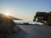 a sunset view from behind the road with a person riding a bike along the shore