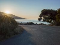 a sunset view from behind the road with a person riding a bike along the shore