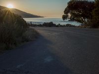 a sunset view from behind the road with a person riding a bike along the shore