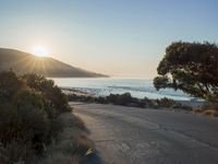a sunset view from behind the road with a person riding a bike along the shore