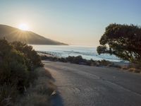 a sunset view from behind the road with a person riding a bike along the shore