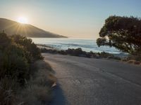 a sunset view from behind the road with a person riding a bike along the shore