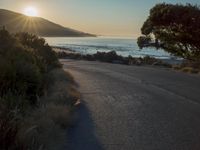 a sunset view from behind the road with a person riding a bike along the shore