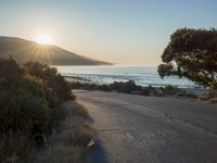 a sunset view from behind the road with a person riding a bike along the shore