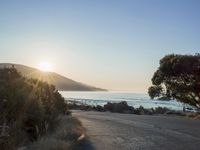 a sunset view from behind the road with a person riding a bike along the shore