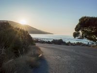 a sunset view from behind the road with a person riding a bike along the shore