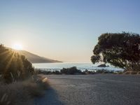 a sunset view from behind the road with a person riding a bike along the shore