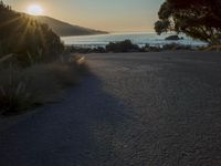 a sunset view from behind the road with a person riding a bike along the shore