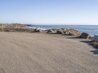 a parking lot overlooking the ocean with three large rocks in the background and two smaller rocks at the far end of the road