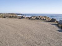 a parking lot overlooking the ocean with three large rocks in the background and two smaller rocks at the far end of the road