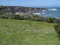 the shore line and grassy green cliff face at the ocean's edge, with cliffs on the far side