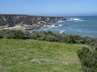 the shore line and grassy green cliff face at the ocean's edge, with cliffs on the far side