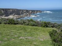 the shore line and grassy green cliff face at the ocean's edge, with cliffs on the far side