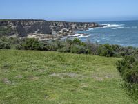 the shore line and grassy green cliff face at the ocean's edge, with cliffs on the far side