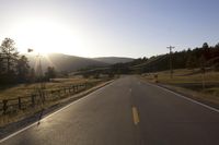 a view down the middle of the road at sunset with mountains and trees in the background
