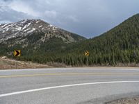 a mountain side with a road running next to the mountains, a bike parked in front of it and trees on one side