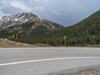 a mountain side with a road running next to the mountains, a bike parked in front of it and trees on one side