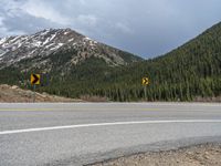 a mountain side with a road running next to the mountains, a bike parked in front of it and trees on one side